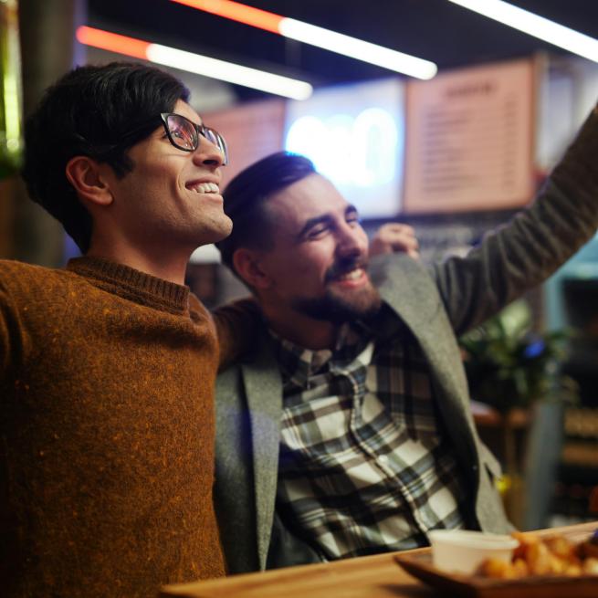 Zwei Männer feiern in einer Bar und sehen beim Fussball zu.
